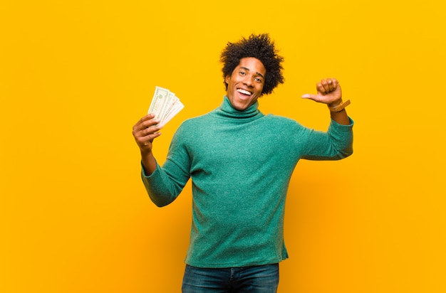 Young african american man with dollar bills against orange back