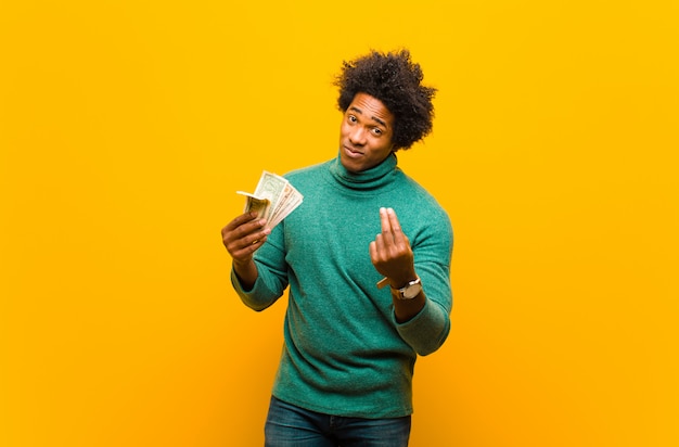 Young african american man with dollar bills against orange back