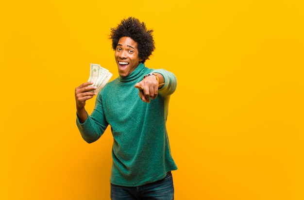 Young african american man with dollar bills against orange