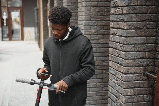 Young african-american man with electric scooter in the city