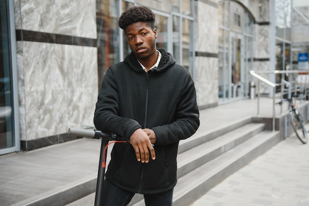 young african-american man with electric scooter in the city