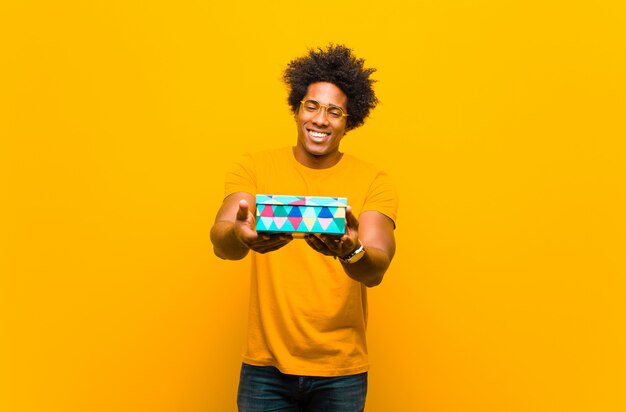 Young african american man with a gift box against orange