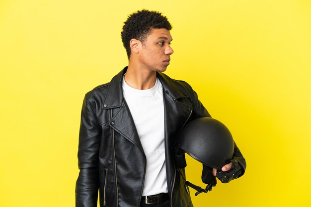 Young African American man with a motorcycle helmet isolated on yellow background looking to the side