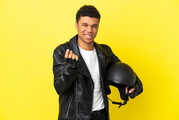 Young African American man with a motorcycle helmet isolated on yellow background making money gesture