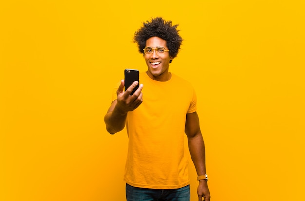 Young african american man with a smart phone against orange bac