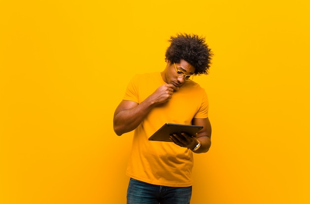 Young african american man with a tablet against orange backgrou