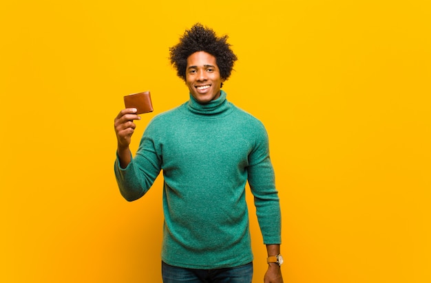 Young african american man with a wallet against orange backgrou