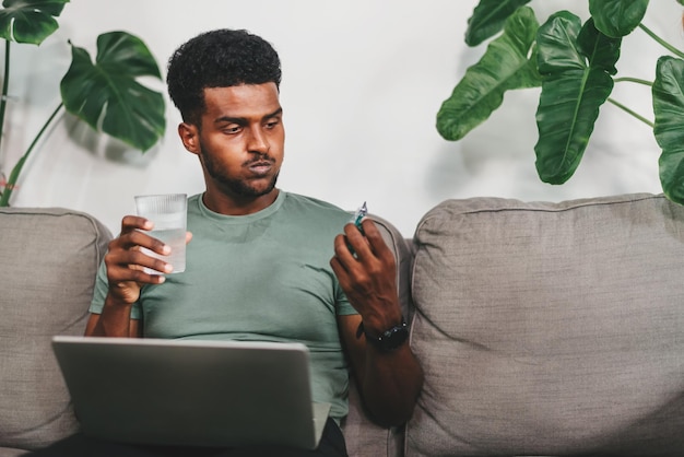 写真 リビングルームでの仕事のためにラップトップコンピューターを使用して自宅で働く若いアフリカ系アメリカ人男性頭痛治療オンライン医療相談への予約