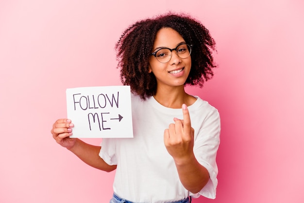 Young african american mixed race woman holding a follow me concept pointing with finger at you as if inviting come closer.