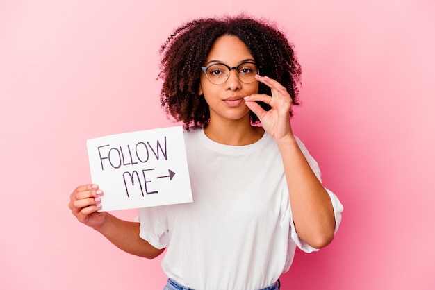 Young african american mixed race woman holding a follow me concept with fingers on lips keeping a secret.