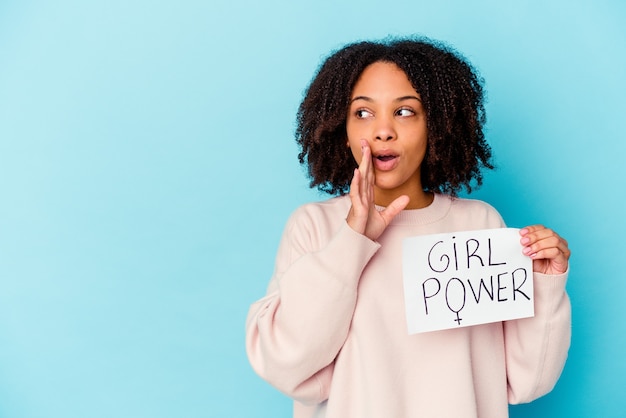 Young african american mixed race woman holding a girl power concept is saying a secret hot braking news and looking aside