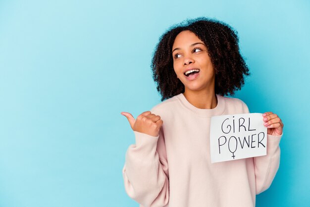 Young african american mixed race woman holding a girl power concept points with thumb finger away, laughing and carefree.