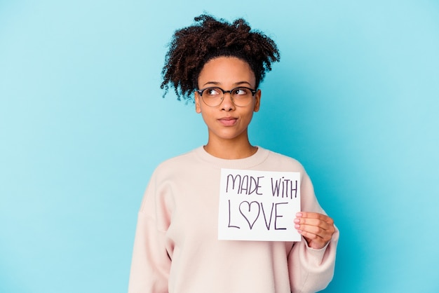 Young african american mixed race woman holding a made with love concept confused, feels doubtful and unsure.