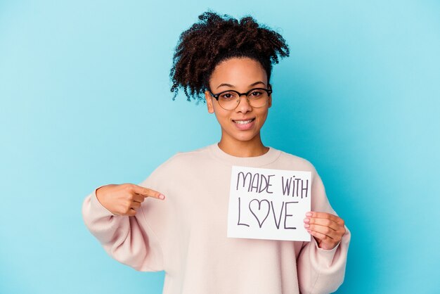 Young african american mixed race woman holding a made with love concept person pointing by hand to a shirt copy space, proud and confident