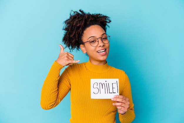 Giovane donna afroamericana di razza mista che tiene un concetto di sorriso che mostra un gesto di chiamata di telefono cellulare con le dita