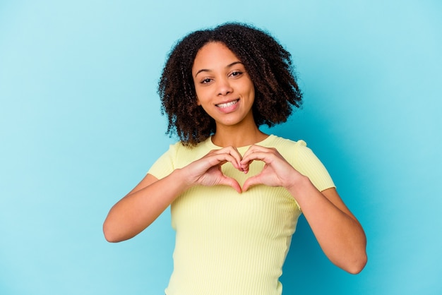 Young african american mixed race woman isolated smiling and showing a heart shape with hands.