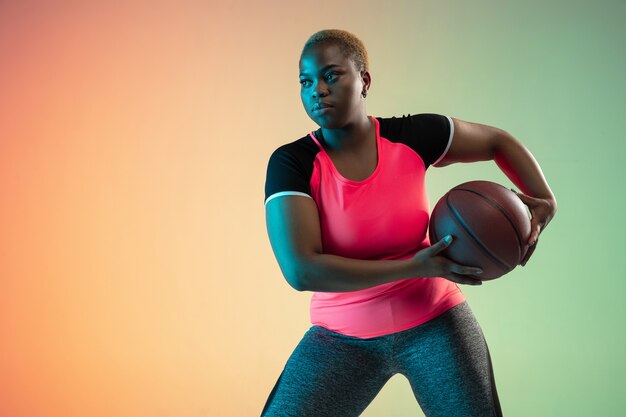 Young african-american plus size female model's training on gradient background