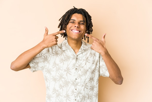 Young african american rasta man smiles, pointing fingers at mouth.