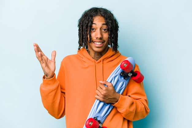 Young African American skater man isolated on blue background receiving a pleasant surprise excited and raising hands