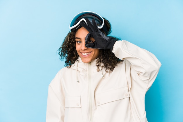 Young african american skier womanexcited keeping ok gesture on eye.