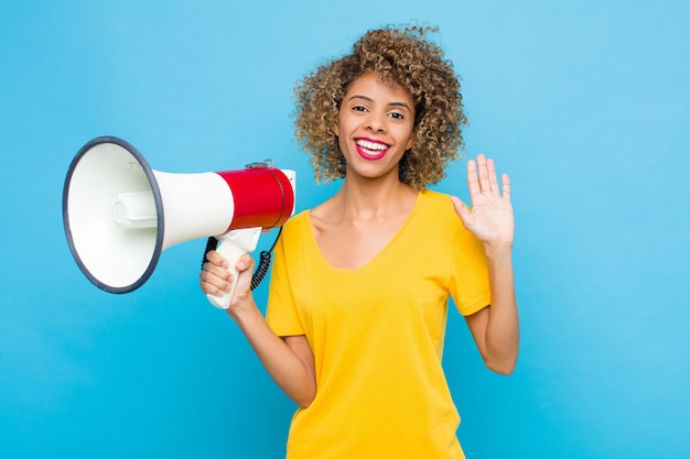 Young african american smiling happily and cheerfully, waving hand, welcoming and greeting you, or saying goodbye with  a megaphone