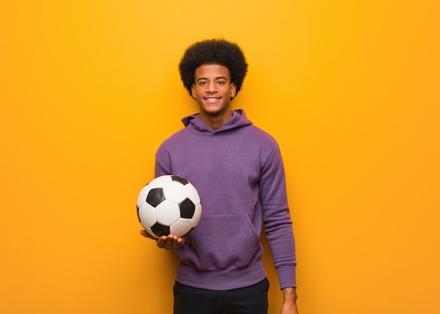 Young african american sport man holding a soccer ball cheerful with a big smile