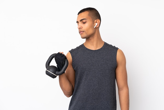 Young African American sport man over isolated white wall making weightlifting with kettlebell