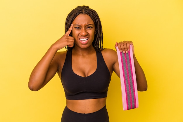Young african american sport woman holding a elastic band isolated on yellow background  showing a disappointment gesture with forefinger.