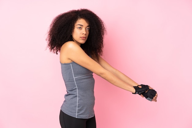 Young african american sport woman isolated on pink stretching