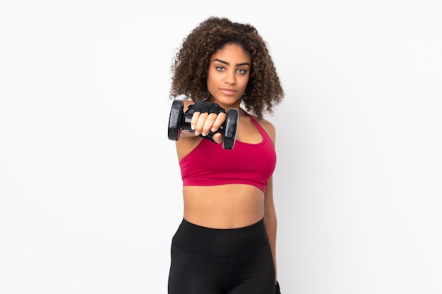 Young African American sport woman on white wall making weightlifting