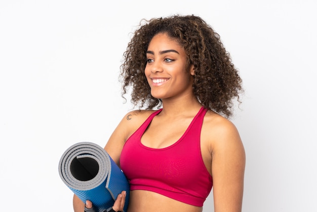 Young African American sport woman on white wall with a mat