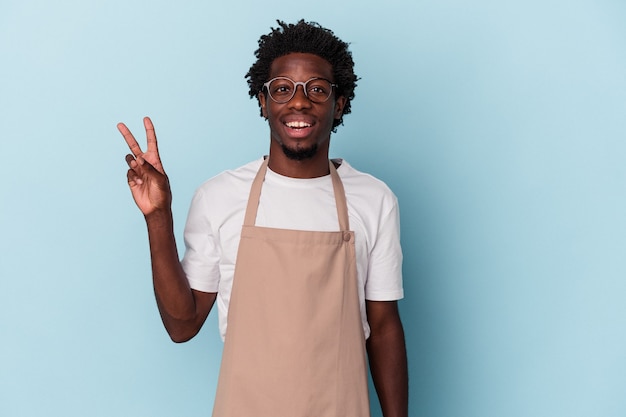 Young african american store clerk isolated on blue background joyful and carefree showing a peace symbol with fingers.