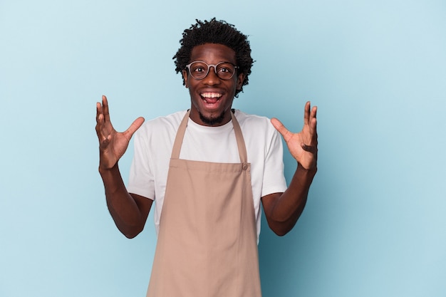 Photo young african american store clerk isolated on blue background receiving a pleasant surprise, excited and raising hands.