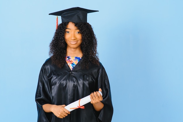 Young African-American student in bachelor robe on color background