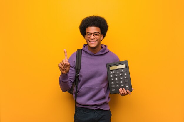 Young african american student man holding a calculator showing number one