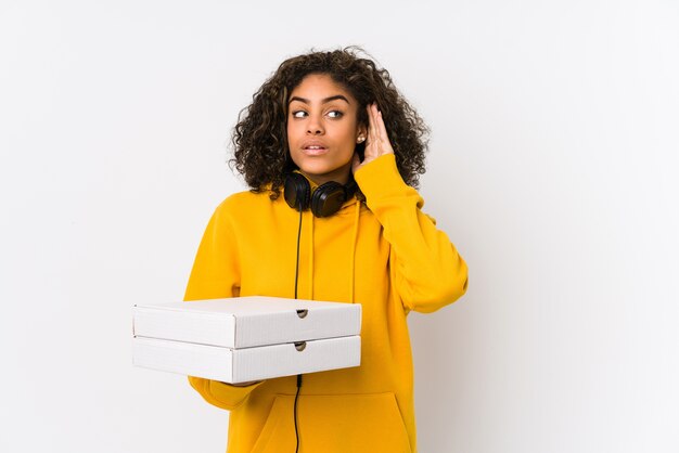 Young african american student woman holding pizzas trying to listening a gossip.