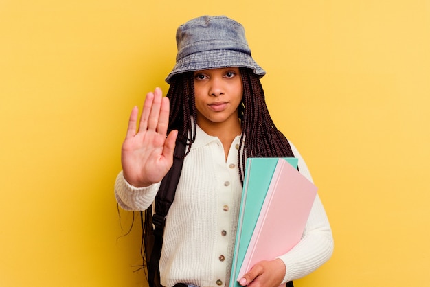 Foto giovane donna afroamericana studentessa isolata su sfondo giallo in piedi con la mano tesa che mostra il segnale di stop, impedendoti.
