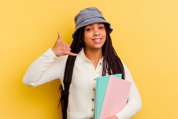 Young african american student woman isolated on yellow showing a mobile phone call gesture with fingers.