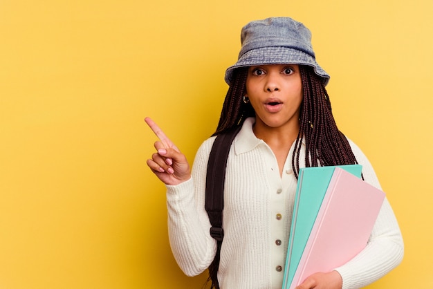 Young african american student woman isolated on yellow wall pointing to the side