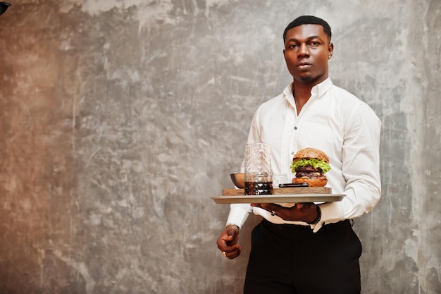 Young african american waiter man hold tray with burger against gray wall