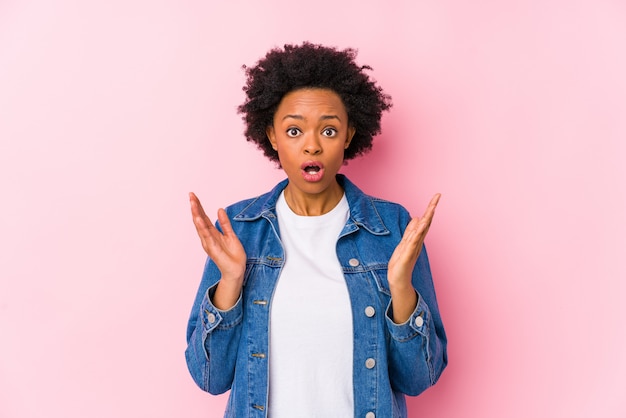 La giovane donna afroamericana contro un backgroound rosa ha isolato sorpreso e colpito.