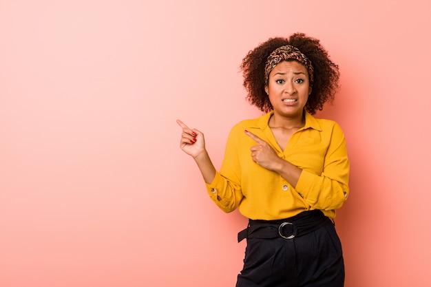 La giovane donna afroamericana contro un fondo rosa ha colpito indicare indicando con i dito indice uno spazio della copia.