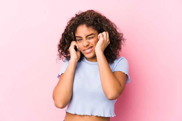 Young african american woman against a pink space covering ears with hands.