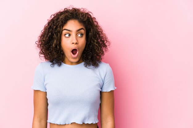 Young african american woman against a pink wall being shocked because of something she has seen.