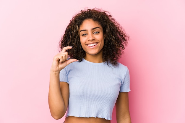 笑顔と自信を持って、人差し指で少し何かを保持しているピンクの壁に若いアフリカ系アメリカ人女性。