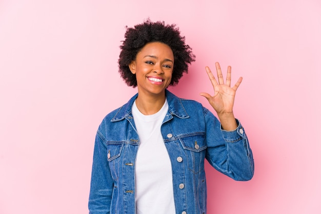 Young african american woman against a pink wall isolated smiling cheerful showing number five with fingers.