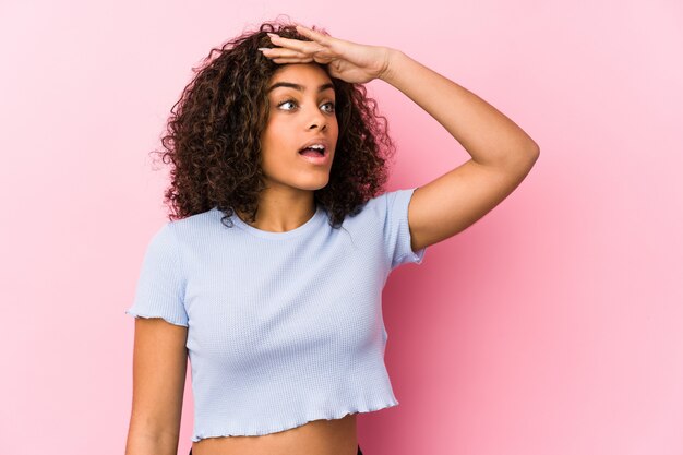 Young african american woman against a pink wall looking far away keeping hand on forehead.