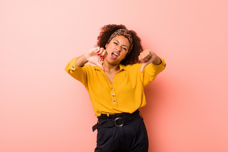 Photo young african american woman against a pink wall showing thumb down and expressing dislike.
