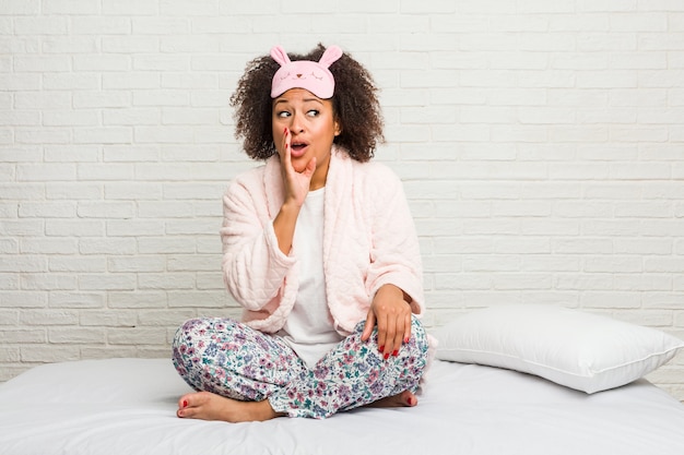 Young african american woman in the bed wearing pijama is saying a secret hot braking news and looking aside