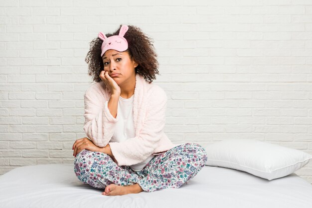 Young african american woman in the bed wearing pijama who is bored, fatigued and need a relax day